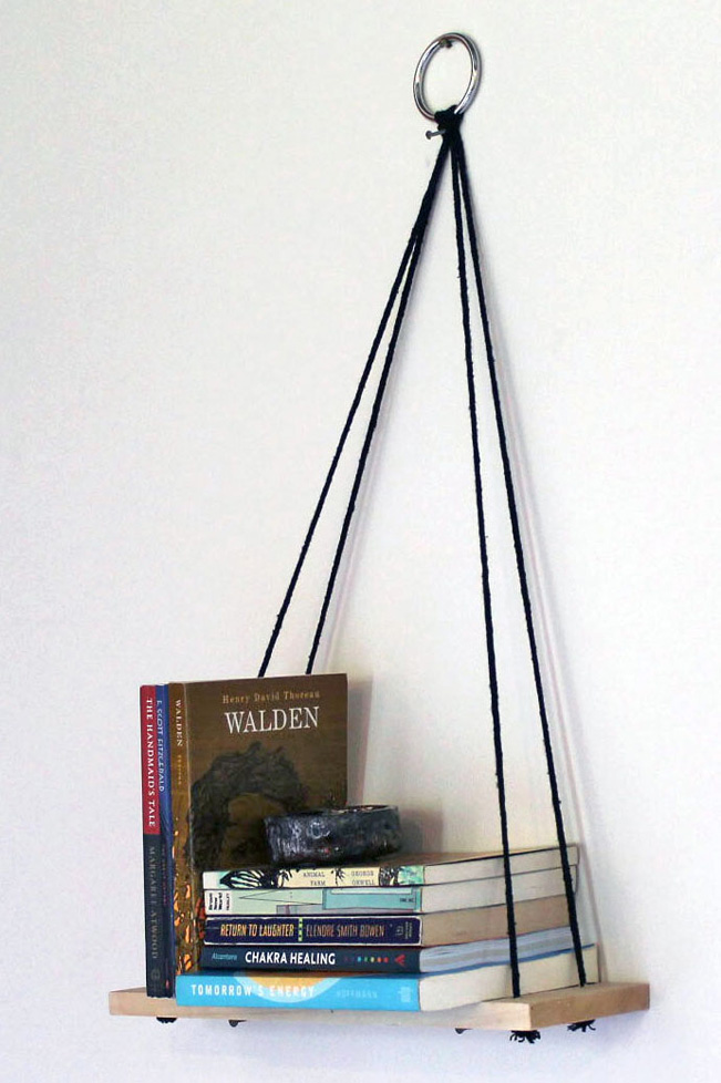 small bookshelf suspended from black chords attached to a ring on the wall