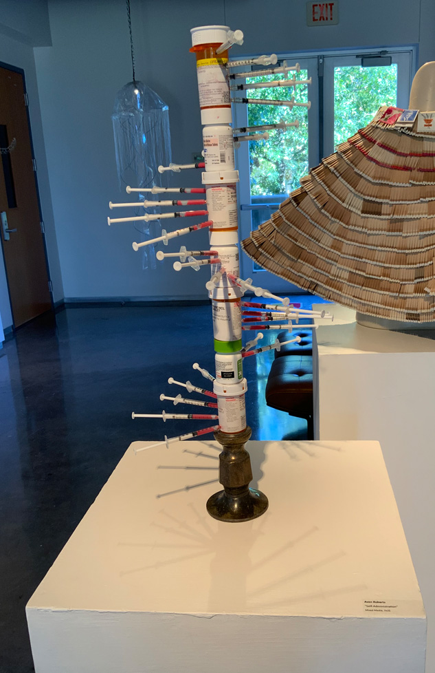 sculpture: tower of pill bottles with spiral of syringes