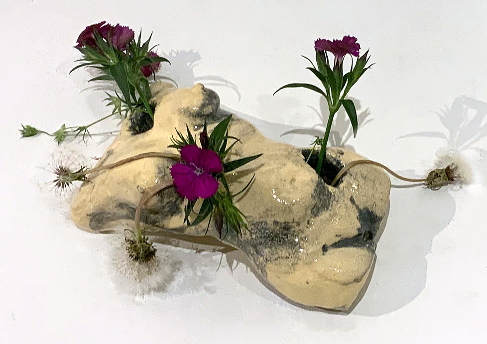 ceramic torso lying prone with flowers in holes in shoulder and abdomen, like a vase