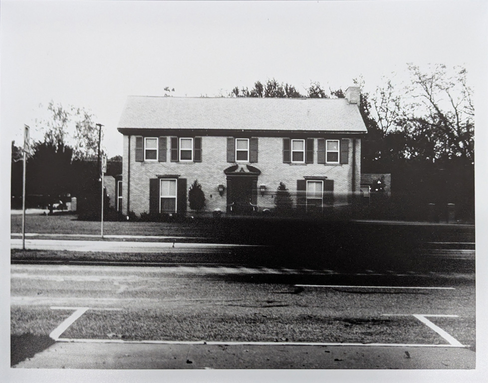 b&w photo of house with blurred car driving in front