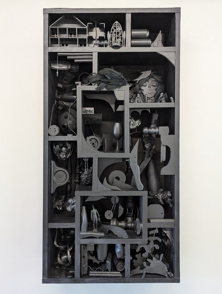 found-object sculpture of various items all painted black inside shelf of black cubbies