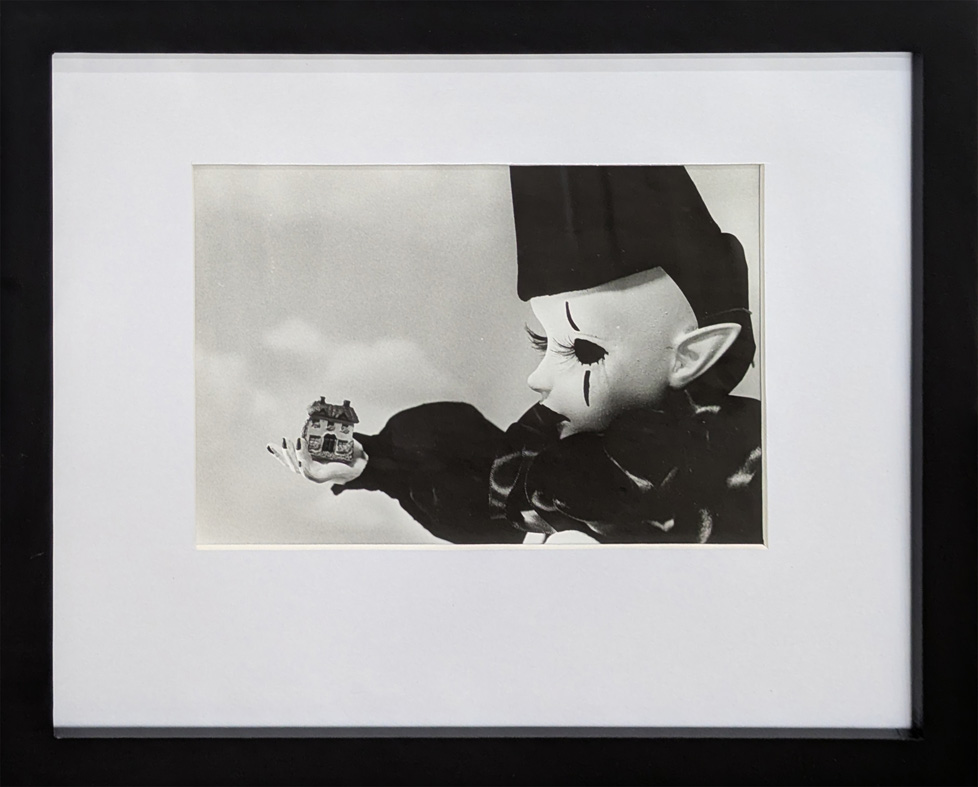 b/w photo of clown doll holding tiny house