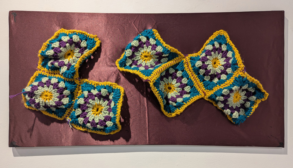 yellow, blue, purple, and white potholders stitched together on stretched purple fabric
