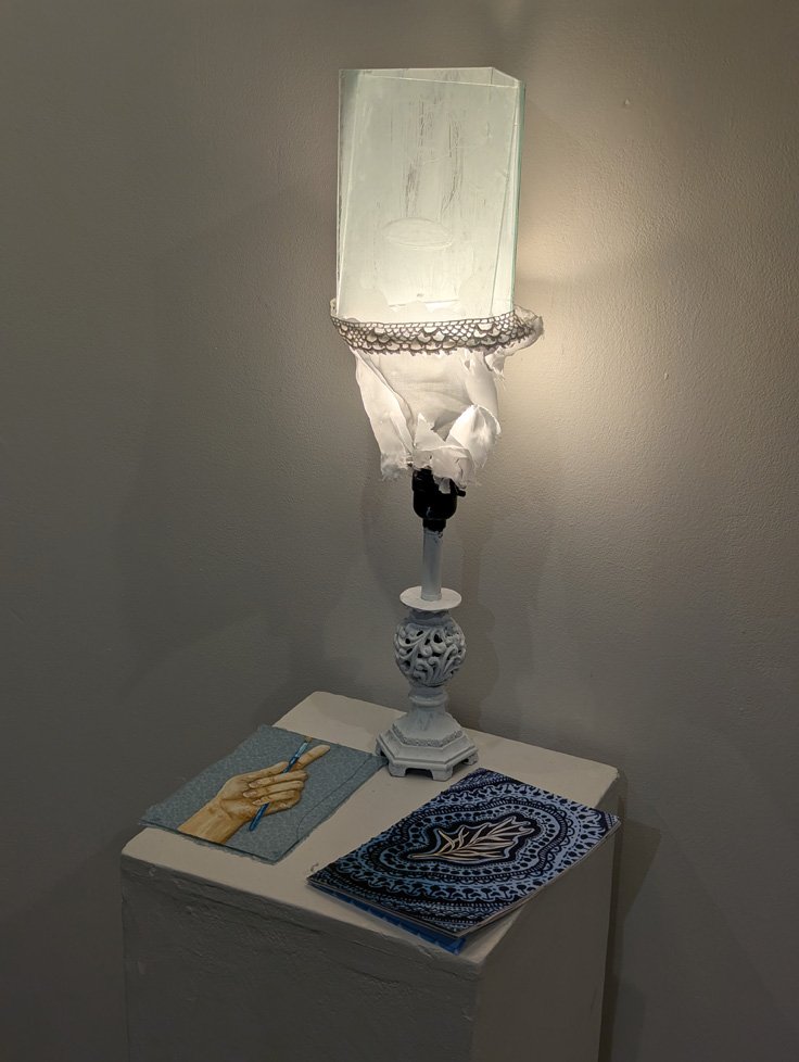 lamp on pedestal with painting of hand holding brush and booklet