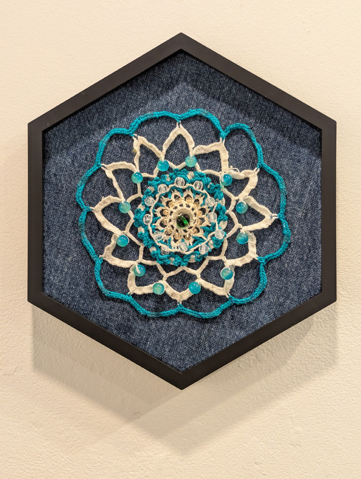 blue and white crocheted lace with beads pinned to blue fabric stretched and framed in hexagon