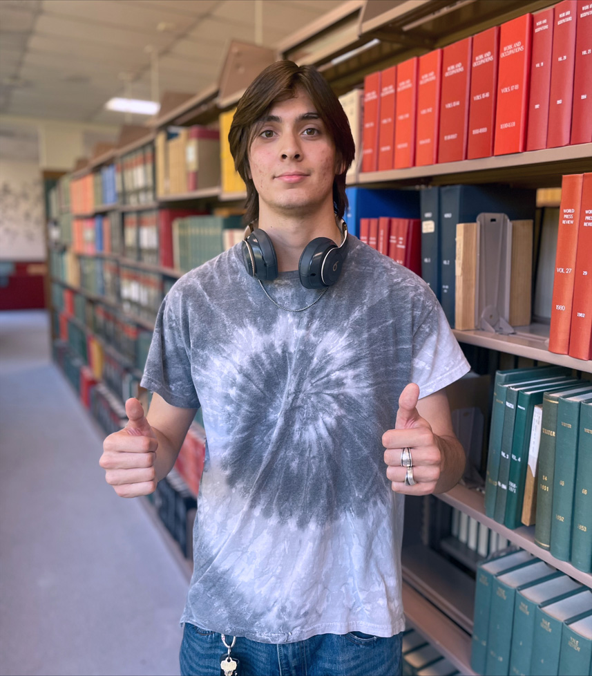 Mitchell, 2 thumbs up, with headphones and tie die shirt in library
