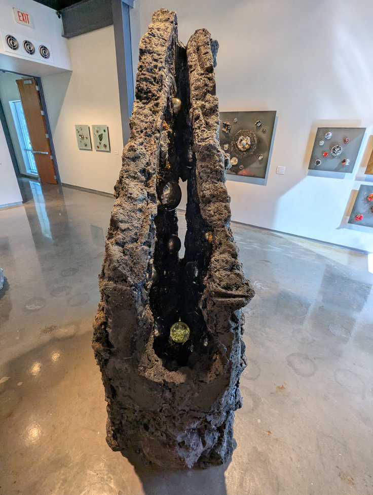 2nd view of geometric rock sculpture showing split in middle with geode-like mirrored balls inside and a glowing orb at the bottom